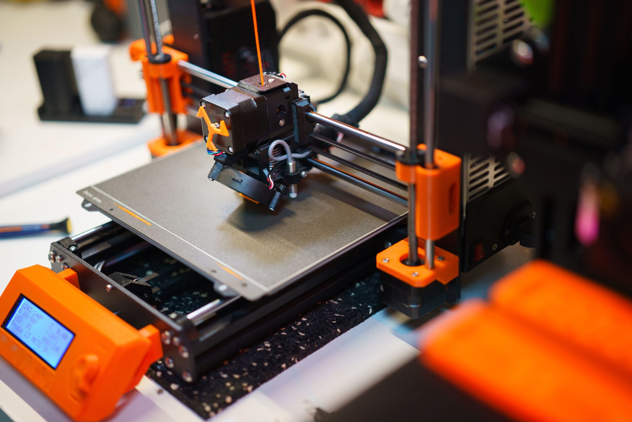 Home Detailed view of a 3D printer creating an object with orange components.