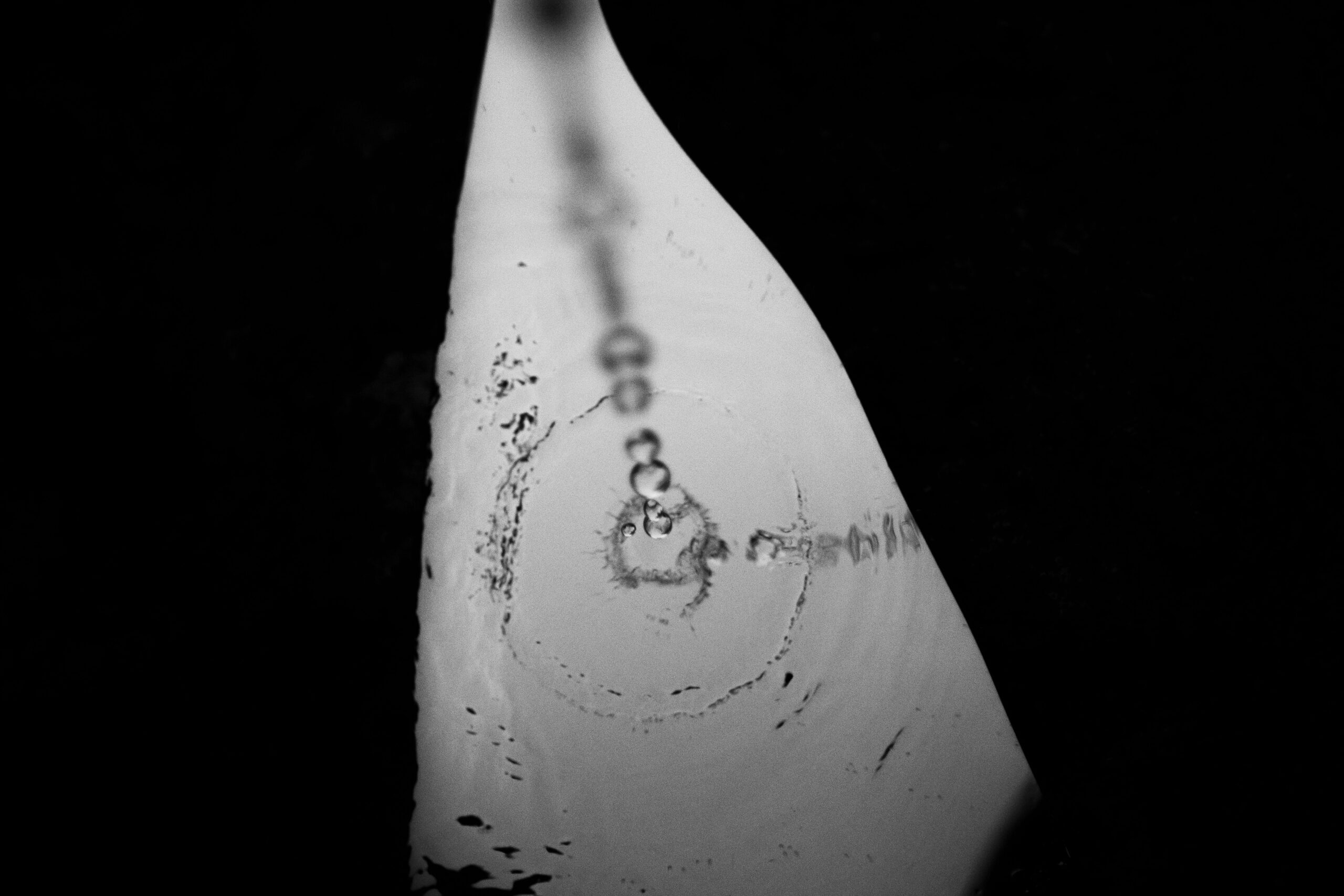 Black and white top view of clear puddle with droplets of water on dark street with shadow in evening time